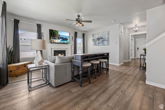 7886 N Bridleway Rd, Eagle Mountain, UT 84005 - living room featuring a ceiling fan, wood finished floors, a glass covered fireplace, baseboards, and a textured ceiling