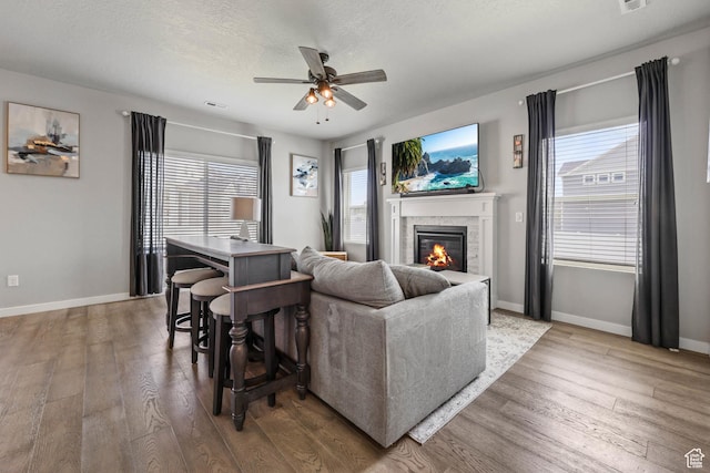 7886 N Bridleway Rd, Eagle Mountain, UT 84005 - living area featuring hardwood / wood-style floors, a glass covered fireplace, ceiling fan, baseboards, and plenty of natural light