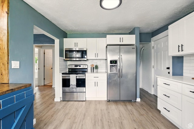 148 E 200 S, Providence, UT 84332 - kitchen featuring appliances with stainless steel finishes, light wood finished floors, tasteful backsplash, white cabinets, and a textured ceiling