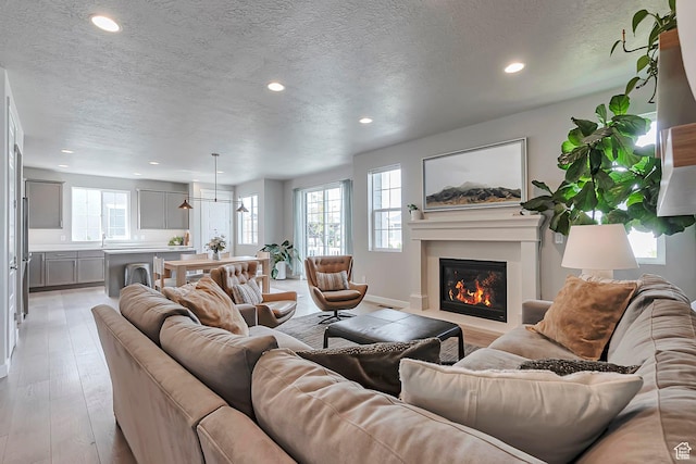 3864 W Safflower Dr, Lehi, UT 84043 - living room with a textured ceiling, a glass covered fireplace, recessed lighting, and light wood-style flooring