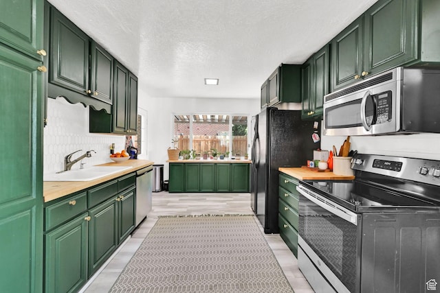 2890 Wheelock Ave, Ogden, UT 84403 - kitchen featuring appliances with stainless steel finishes, green cabinets, a sink, backsplash, and light wood-style floors