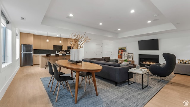 14708 S Woods Landing Ct E, Draper, UT 84020 - dining room featuring a raised ceiling, light wood-style flooring, recessed lighting, a lit fireplace, and baseboards