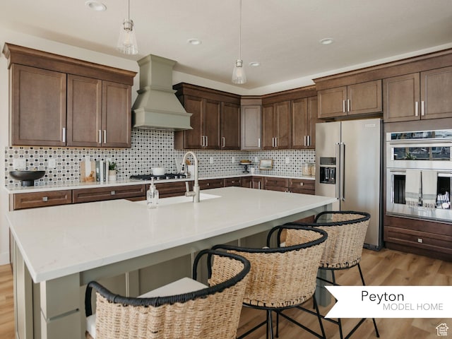 1549 W Boseman Way Unit 601, Saratoga Springs, UT 84045 - kitchen featuring appliances with stainless steel finishes, premium range hood, a kitchen bar, light wood-style floors, and hanging light fixtures
