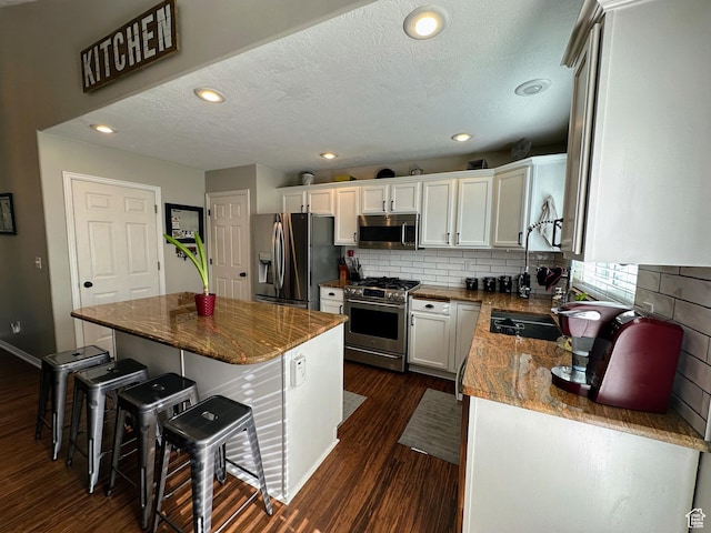 8675 S Pebblecreek Rd, West Jordan, UT 84081 - kitchen featuring appliances with stainless steel finishes, dark wood-style floors, a breakfast bar area, tasteful backsplash, and a textured ceiling