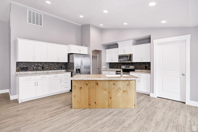 818 S 560 E, Providence, UT 84332 - kitchen with appliances with stainless steel finishes, backsplash, a center island with sink, white cabinetry, and light wood-style floors