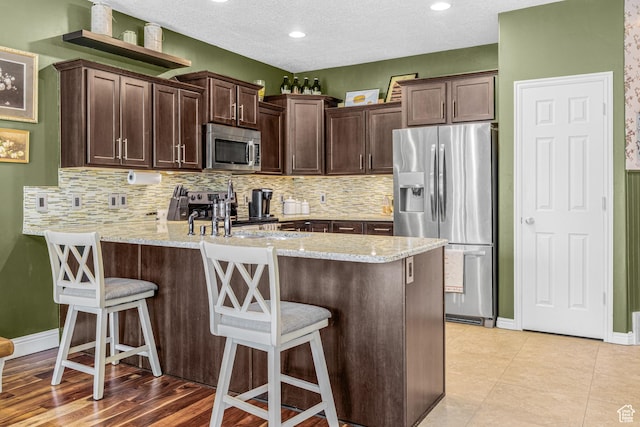 839 W Jordan Oaks Ct S, Sandy, UT 84070 - kitchen featuring appliances with stainless steel finishes, a peninsula, dark brown cabinetry, tasteful backsplash, and a textured ceiling