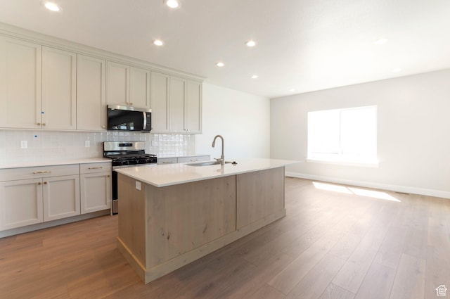 2133 N 725 W, Centerville, UT 84014 - kitchen with appliances with stainless steel finishes, a sink, decorative backsplash, a center island with sink, and light wood finished floors