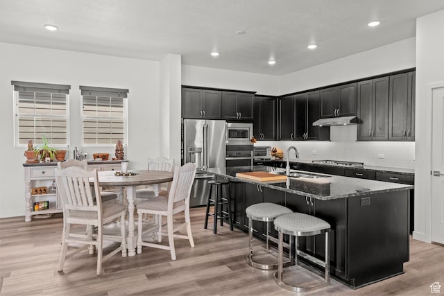 11242 S Willow Dr, South Jordan, UT 84009 - kitchen featuring stainless steel appliances, a sink, dark cabinetry, under cabinet range hood, and dark stone countertops