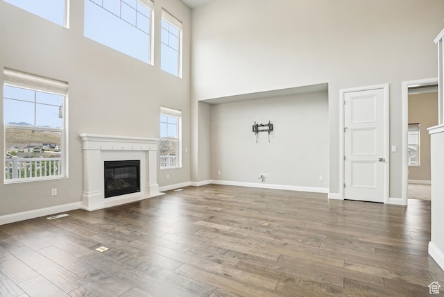 15056 S Sage Terrace Ln Unit 1014, Herriman, UT 84096 - unfurnished living room featuring a towering ceiling, healthy amount of natural light, a glass covered fireplace, wood finished floors, and baseboards