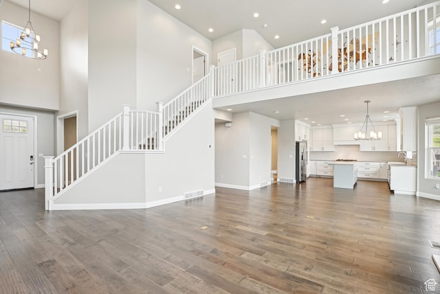 15056 S Sage Terrace Ln Unit 1014, Herriman, UT 84096 - unfurnished living room featuring a chandelier, a towering ceiling, a sink, stairway, and dark wood-type flooring