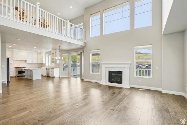 15056 S Sage Terrace Ln Unit 1014, Herriman, UT 84096 - unfurnished living room featuring wood finished floors, a towering ceiling, a glass covered fireplace, baseboards, and recessed lighting
