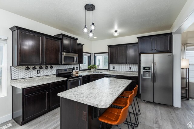 15187 S Sabre Pl, Bluffdale, UT 84065 - kitchen featuring stainless steel appliances, light wood-type flooring, decorative backsplash, a kitchen island, and a textured ceiling