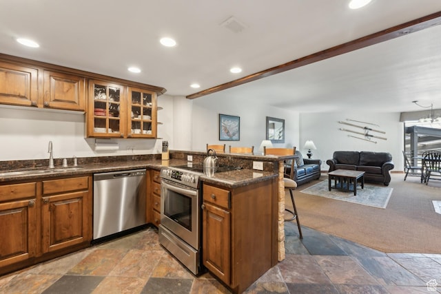 1485 Empire Ave Unit 201, Park City, UT 84060 - kitchen with stainless steel appliances, a sink, brown cabinetry, a kitchen breakfast bar, and stone tile flooring