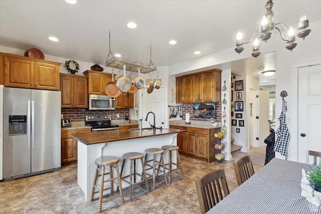 255 W 2700 N Unit 31, Pleasant View, UT 84414 - kitchen with stainless steel appliances, a sink, brown cabinetry, decorative backsplash, and a center island with sink