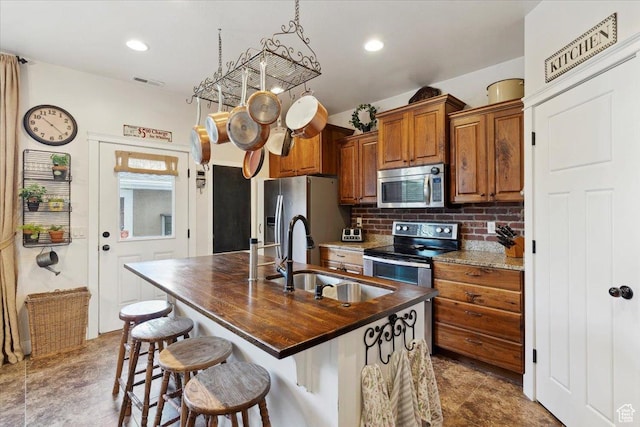 255 W 2700 N Unit 31, Pleasant View, UT 84414 - kitchen featuring appliances with stainless steel finishes, a sink, brown cabinetry, decorative backsplash, and a kitchen island with sink