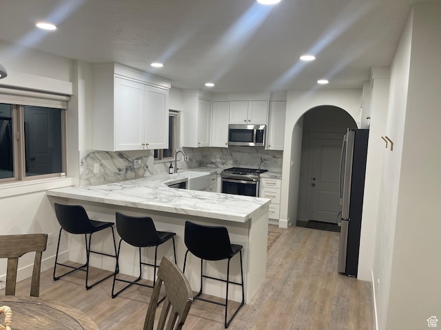 1136 E 3580 S, Millcreek, UT 84106 - kitchen with appliances with stainless steel finishes, a peninsula, white cabinetry, a kitchen bar, and tasteful backsplash