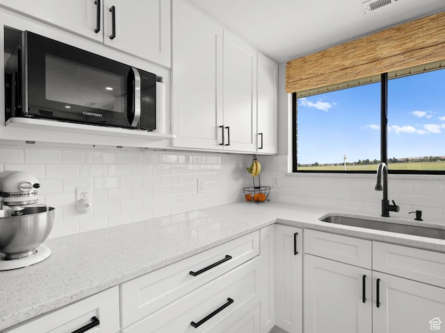 1491 Bryan Rd, Erda, UT 84074 - kitchen with black microwave, a sink, tasteful backsplash, white cabinetry, and light stone countertops