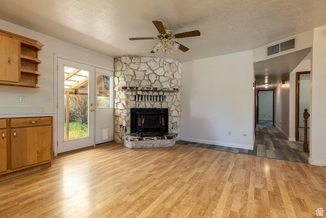 437 S 100 W, Kanab, UT 84741 - unfurnished living room featuring light wood-style floors, a ceiling fan, a textured ceiling, a stone fireplace, and baseboards
