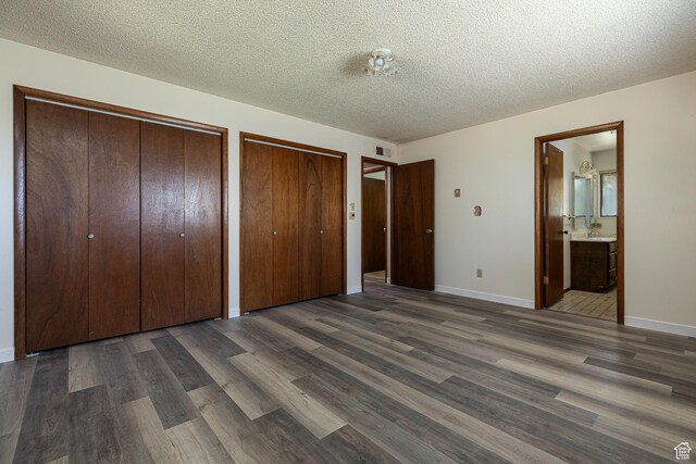 437 S 100 W, Kanab, UT 84741 - unfurnished bedroom featuring two closets, dark wood-style flooring, a textured ceiling, ensuite bathroom, and baseboards