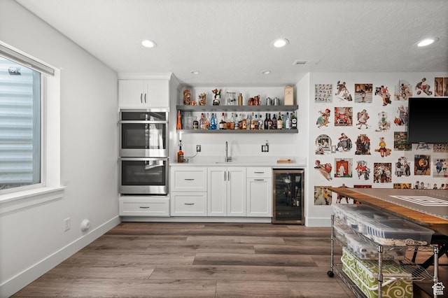 1067 W Ludington Ct, Bluffdale, UT 84065 - indoor wet bar featuring beverage cooler, stainless steel double oven, healthy amount of natural light, recessed lighting, and wood finished floors