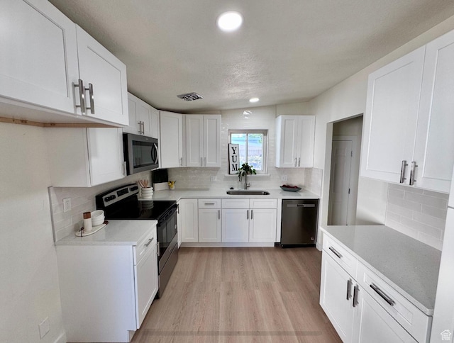 5011 S Leisure Ln W, Taylorsville, UT 84129 - kitchen featuring stainless steel appliances, a sink, white cabinetry, decorative backsplash, and light wood-style floors