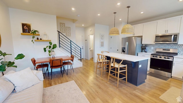 9367 N Vernham Way E, Eagle Mountain, UT 84005 - kitchen with appliances with stainless steel finishes, a breakfast bar, a center island, light wood-type flooring, and white cabinets