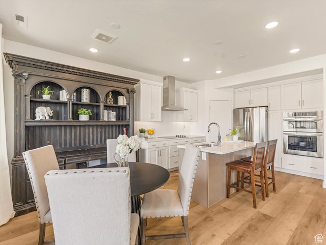 1512 W Fiore St, Farmington, UT 84025 - kitchen with wall chimney range hood, a sink, appliances with stainless steel finishes, a kitchen island with sink, and a breakfast bar area