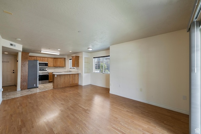 191 E Spencer Peak Way Unit I2, Draper, UT 84020 - kitchen with appliances with stainless steel finishes, open floor plan, light wood-style floors, light countertops, and brown cabinets