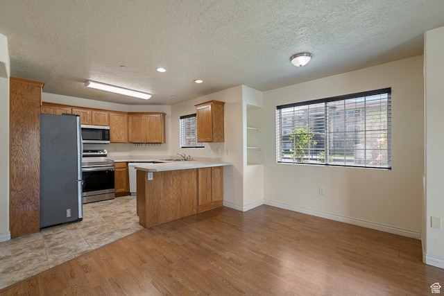 191 E Spencer Peak Way Unit I2, Draper, UT 84020 - kitchen with stainless steel appliances, a peninsula, a textured ceiling, light countertops, and light wood-type flooring