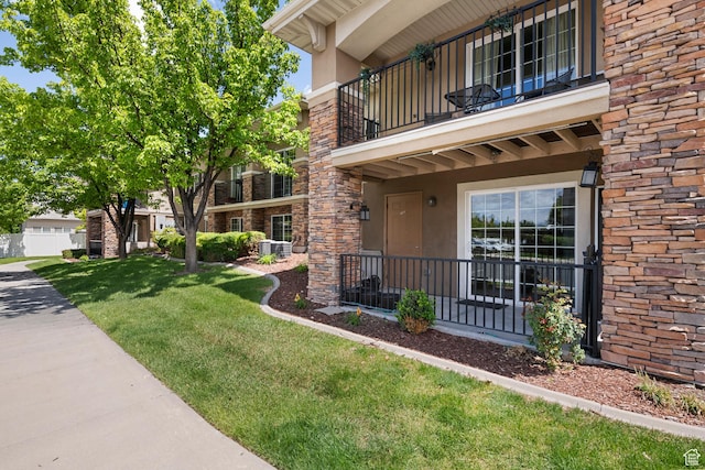 191 E Spencer Peak Way Unit I2, Draper, UT 84020 - view of exterior entry featuring a balcony, a lawn, stucco siding, brick siding, and central air condition unit