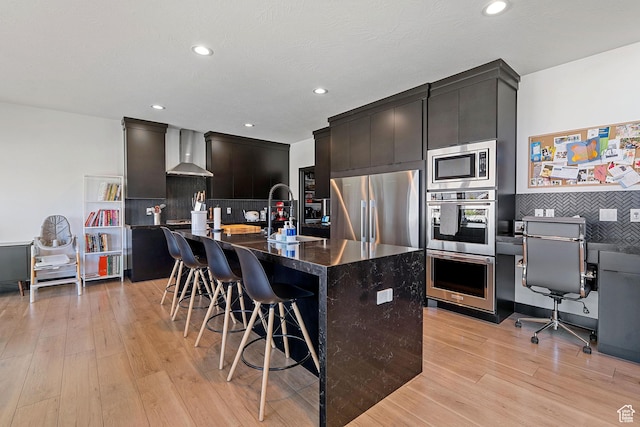 189 N 20 W, Vineyard, UT 84059 - kitchen featuring stainless steel appliances, wall chimney range hood, a sink, light wood-type flooring, and a kitchen breakfast bar