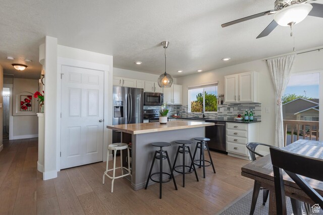 4952 W Buffalo Ct S, Riverton, UT 84096 - kitchen featuring appliances with stainless steel finishes, white cabinetry, a kitchen bar, light wood-style flooring, and recessed lighting