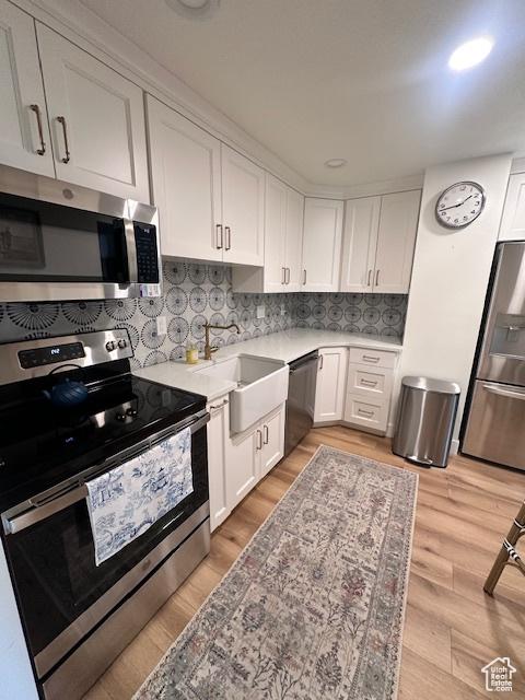 875 S Donner Way E Unit 208, Salt Lake City, UT 84108 - kitchen featuring stainless steel appliances, white cabinetry, a sink, backsplash, and light wood-style floors