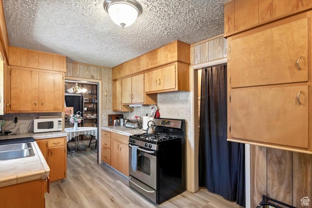 12525 S 1300 E, Draper, UT 84020 - kitchen featuring stainless steel gas range, white microwave, a sink, light wood-type flooring, and decorative backsplash