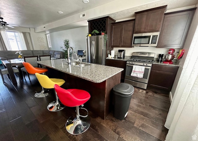 5288 W Solafax Ln Unit 34-1, Herriman, UT 84096 - kitchen with appliances with stainless steel finishes, a sink, dark wood-style flooring, a kitchen island with sink, and dark brown cabinets