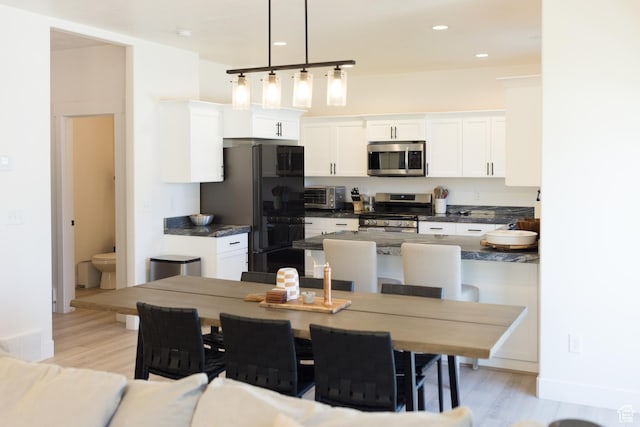 4745 E Silver Moon Dr, Eagle Mountain, UT 84005 - kitchen with stainless steel appliances, dark countertops, light wood finished floors, white cabinets, and decorative light fixtures