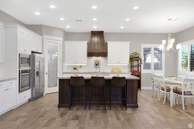 3691 W 2800 S, Hurricane, UT 84737 - kitchen with appliances with stainless steel finishes, custom exhaust hood, a chandelier, an island with sink, and decorative backsplash