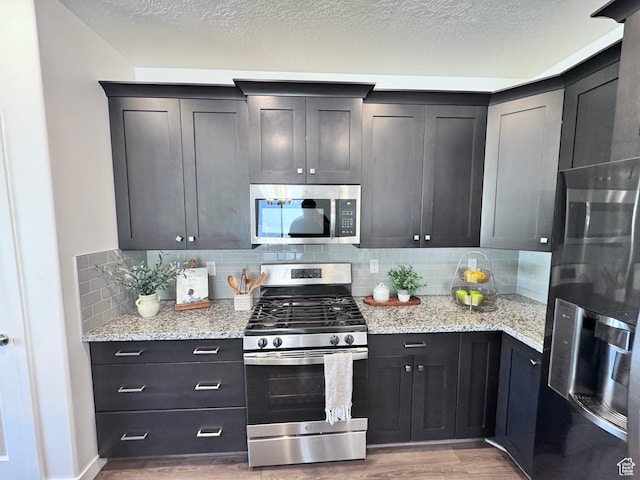 12754 S Quail Lake Dr Unit 126, Riverton, UT 84096 - kitchen featuring stainless steel appliances, light wood-type flooring, tasteful backsplash, light stone countertops, and a textured ceiling