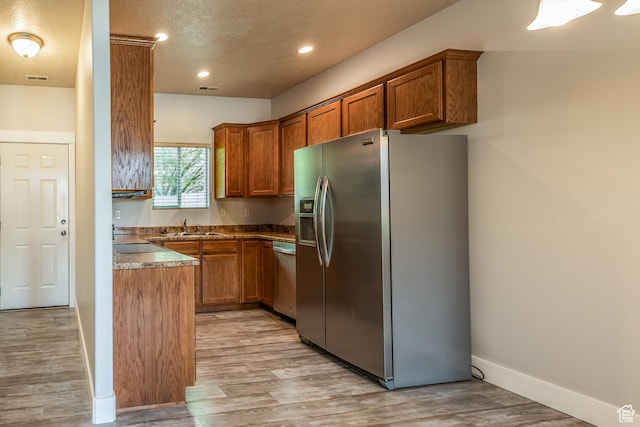 5242 W Cool Water Way S, West Jordan, UT 84081 - kitchen with stainless steel appliances, brown cabinets, a sink, light wood-type flooring, and baseboards