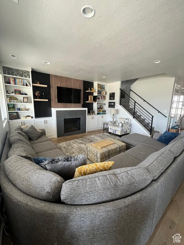 2323 W Thomas Ct, Syracuse, UT 84075 - living room with wood finished floors, a textured ceiling, stairs, a fireplace, and built in shelves