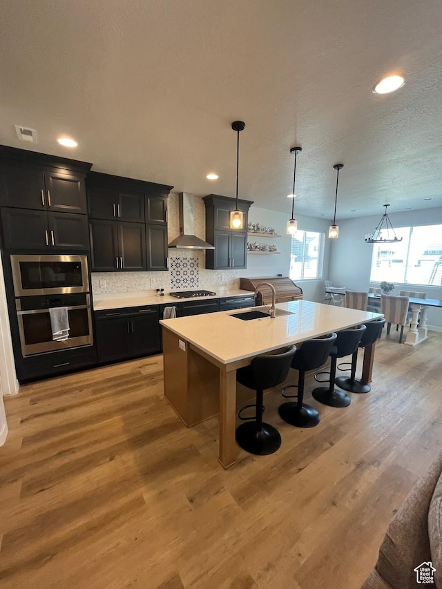 2323 W Thomas Ct, Syracuse, UT 84075 - kitchen featuring wall chimney exhaust hood, a breakfast bar, gas cooktop, dark cabinetry, and light countertops