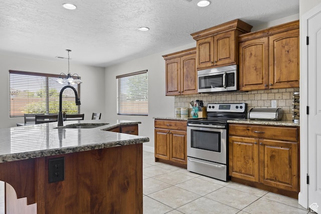 3345 W 2430 S, Hurricane, UT 84737 - kitchen with stainless steel appliances, a sink, decorative backsplash, a chandelier, and brown cabinetry