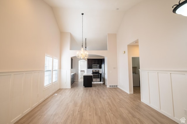 10227 S Oquirrh Lake Rd, South Jordan, UT 84095 - unfurnished living room featuring high vaulted ceiling, a decorative wall, arched walkways, a chandelier, and light wood-style floors
