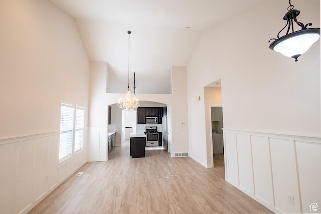 10227 S Oquirrh Lake Rd, South Jordan, UT 84095 - unfurnished living room with high vaulted ceiling, a chandelier, wainscoting, a decorative wall, and light wood-style flooring