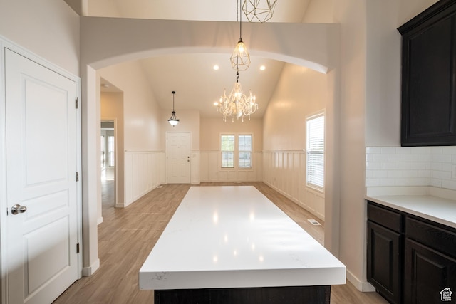 10227 S Oquirrh Lake Rd, South Jordan, UT 84095 - kitchen with wainscoting, arched walkways, light wood-style flooring, dark cabinetry, and lofted ceiling
