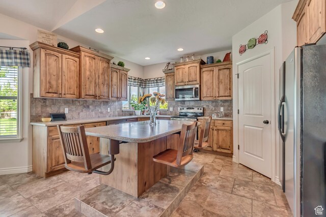 3028 W Viola Ln, Riverton, UT 84065 - kitchen featuring appliances with stainless steel finishes, tasteful backsplash, a center island, light countertops, and a breakfast bar area