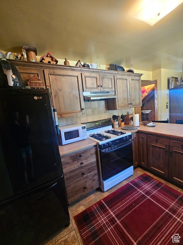 45465 W Airport Rd, Fruitland, UT 84027 - kitchen with freestanding refrigerator, white microwave, range with gas stovetop, under cabinet range hood, and light countertops