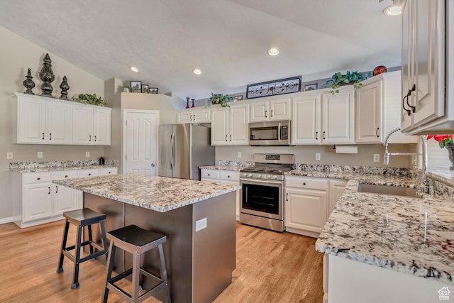 11743 S Silver Spur Ln, Draper, UT 84020 - kitchen with stainless steel appliances, a sink, a breakfast bar area, light wood-style flooring, and white cabinetry