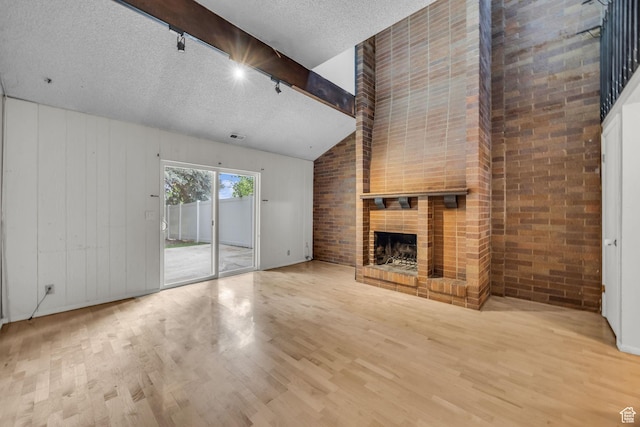 1054 E Lamplighter Dr, River Heights, UT 84321 - unfurnished living room with wood finished floors, a brick fireplace, rail lighting, a textured ceiling, and brick wall