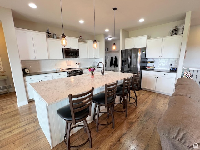 12137 N Montrose Dr, Highland, UT 84003 - kitchen with black appliances, light wood-style floors, backsplash, an island with sink, and a sink